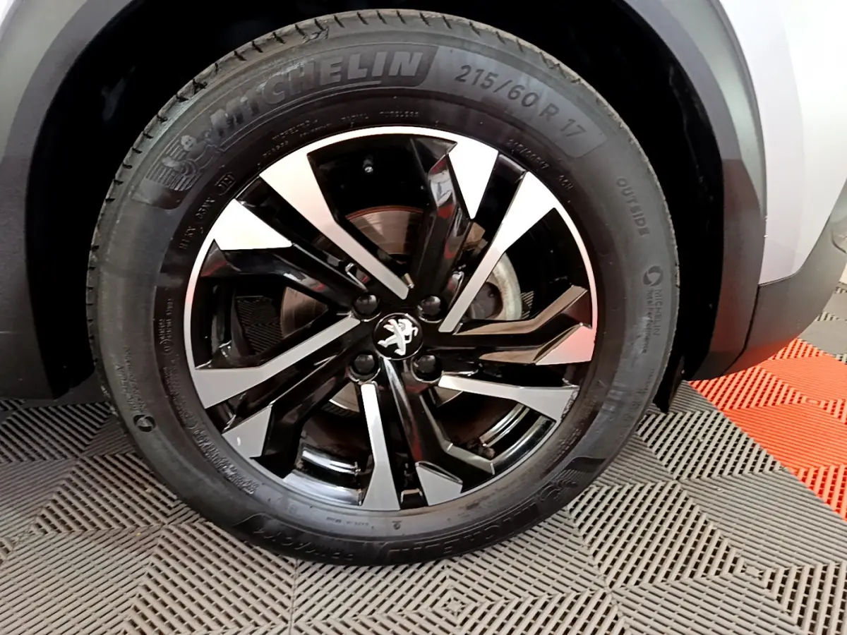 Gros plan sur la roue avant droite du Peugeot 2008 gris clair, jante alliage noire et argentée au design moderne.