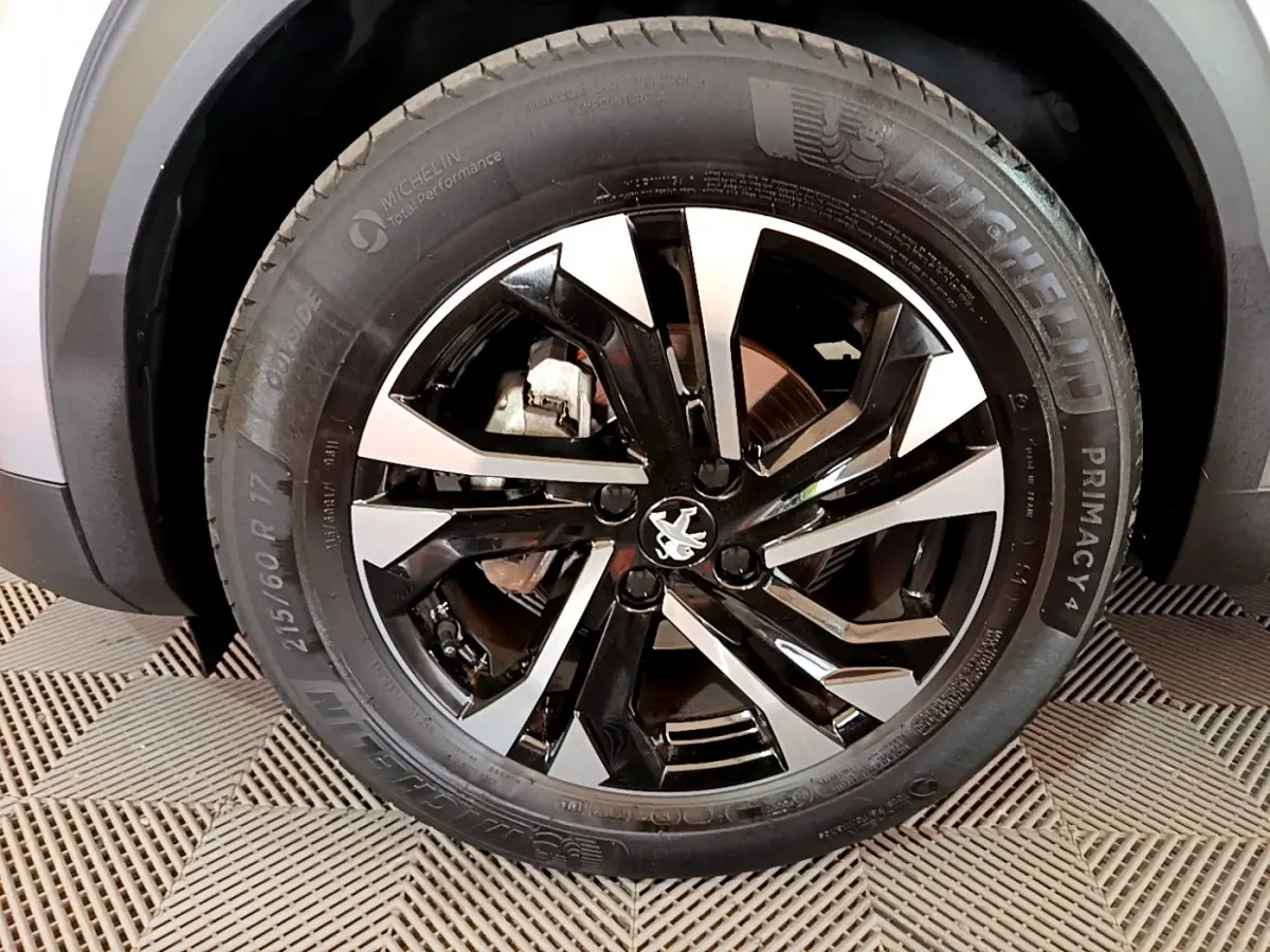 Gros plan sur la roue avant droite du Peugeot 2008 gris clair, jante alliage noire et argent avec logo lion central.