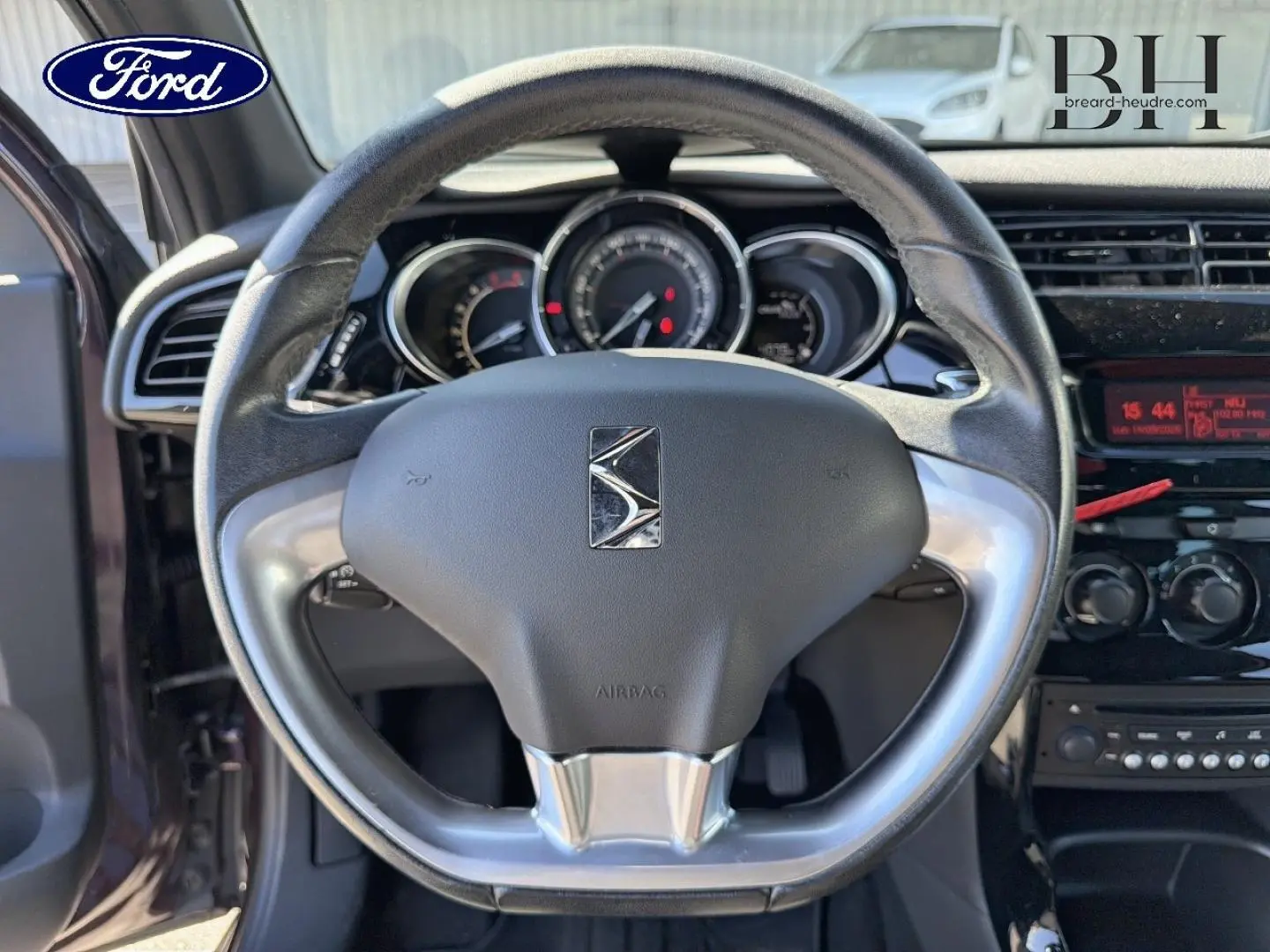 Vue intérieure centrée sur le volant DS3 avec logo Citroën, tableau de bord et console noire brillante.