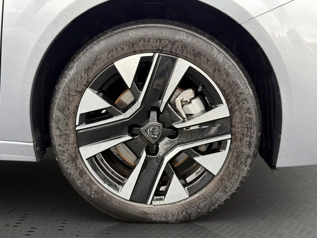 Gros plan sur la roue avant droite d’une Peugeot 208 gris clair, jante alliage bicolore moderne.