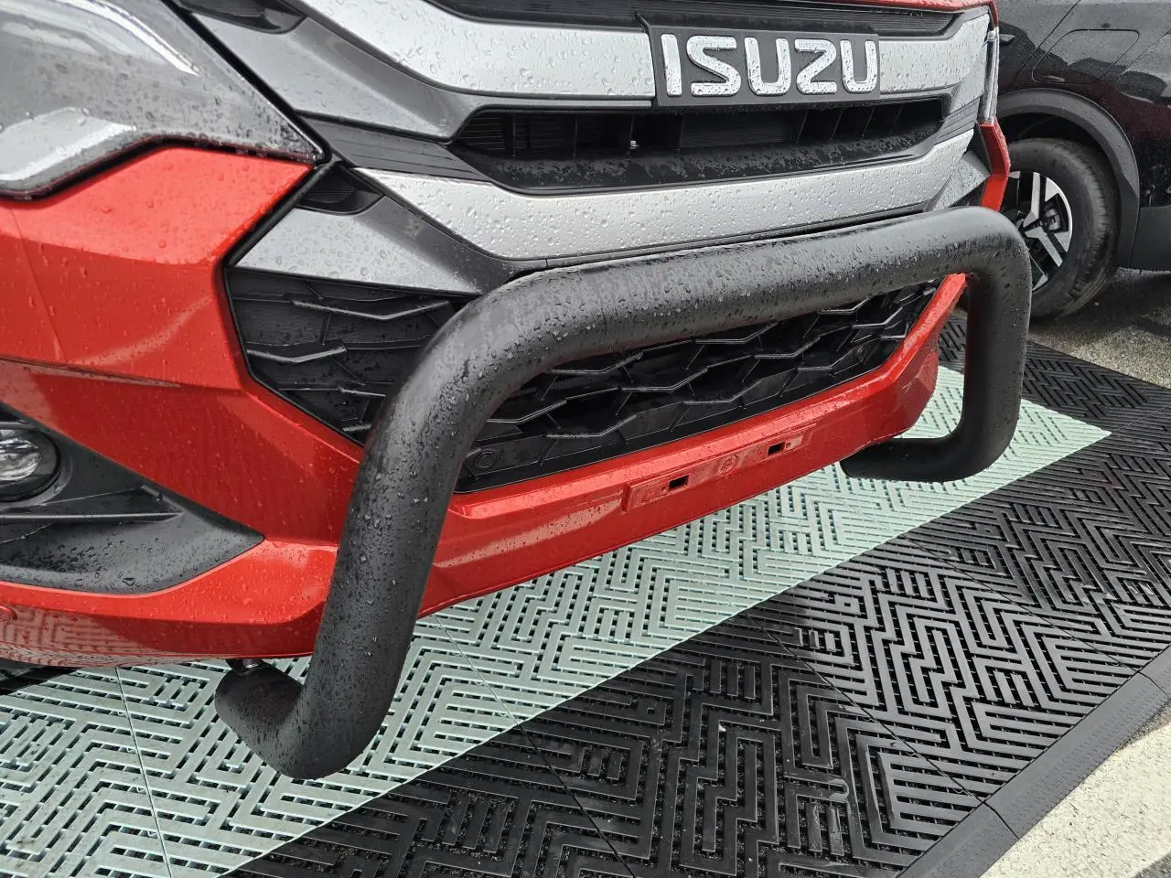 Gros plan sur la face avant orange métallisée d'un Isuzu D-MAX avec bullbar noir et calandre chromée sous la pluie.