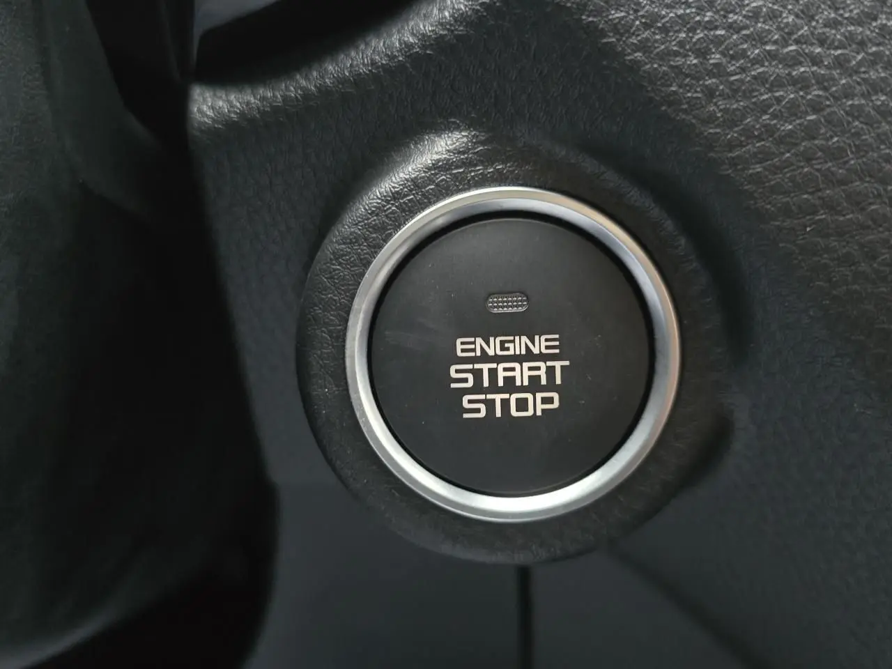 Gros plan sur le bouton noir de démarrage moteur cerclé de chrome dans l'habitacle du pick-up Isuzu D-MAX orange métallisé.