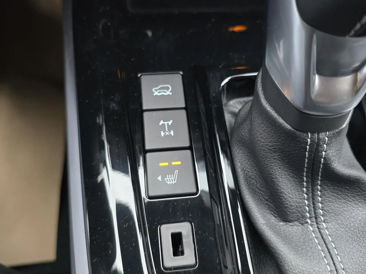 Gros plan sur la console centrale du pick-up Isuzu D-MAX orange, montrant levier de vitesse cuir et boutons de contrôle.