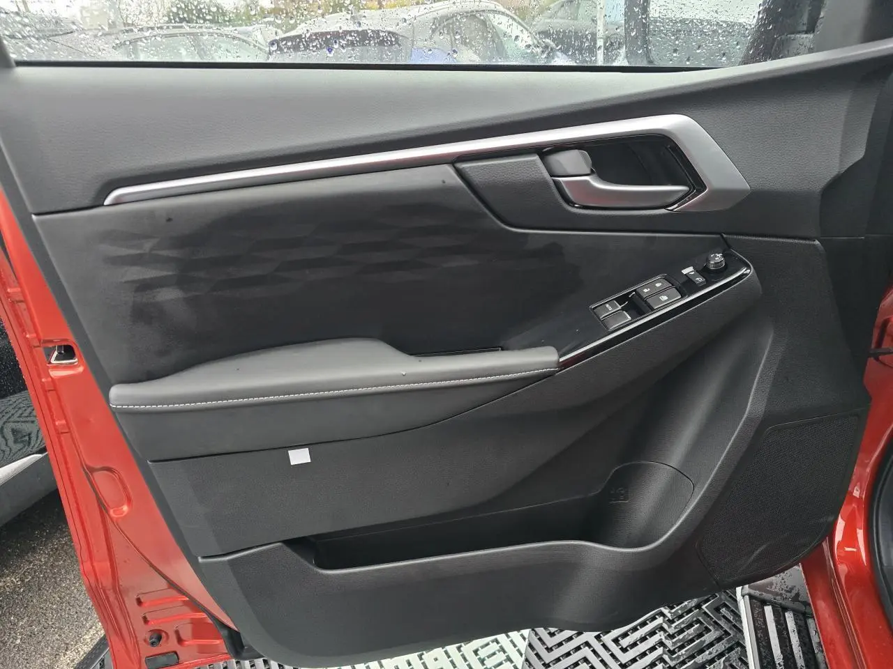 Vue intérieure de la porte côté gauche d'un Isuzu D-MAX orange métallisé avec commandes de vitres et poignée chromée.