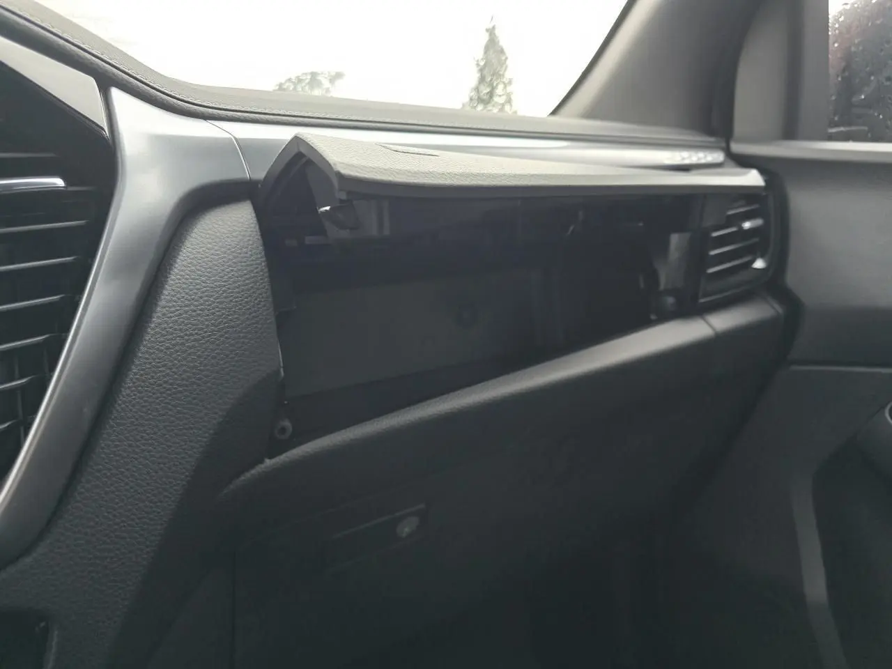 Intérieur du tableau de bord côté passager du pick-up Isuzu D-MAX 2025, avec boîte à gants ouverte et finition noire.