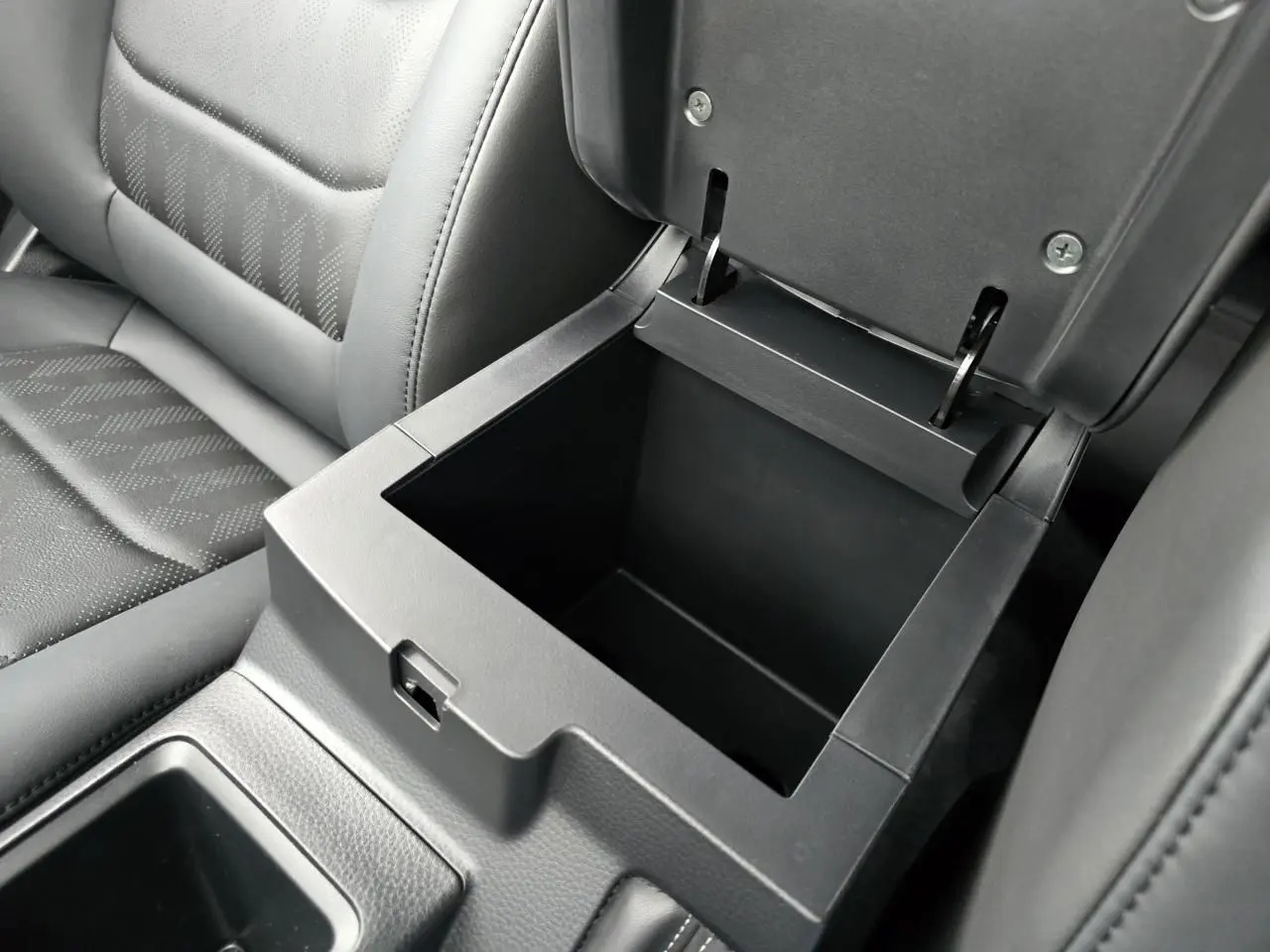 Coffre de rangement central ouvert avec intérieur noir, siège en cuir gris foncé de l'Isuzu D-MAX III NEW 2025.