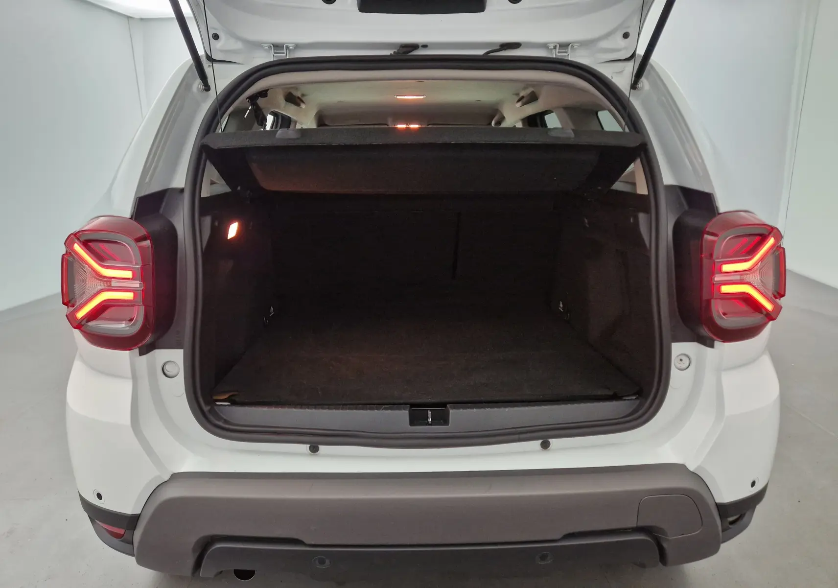 Vue arrière du Dacia Duster blanc 2024 avec coffre ouvert et feux arrière allumés dans un studio lumineux.