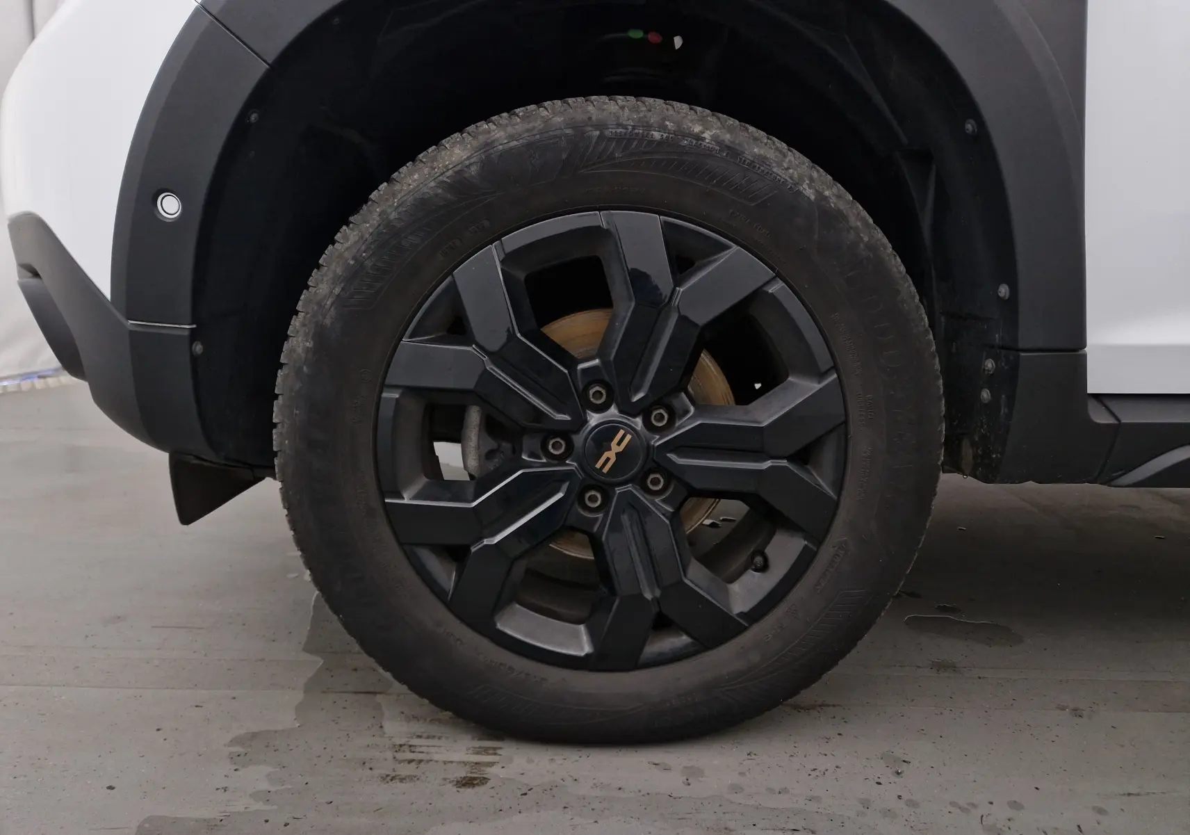 Gros plan sur la roue avant gauche noire du Dacia Duster 4x4 blanc, soulignant la jante au design moderne.