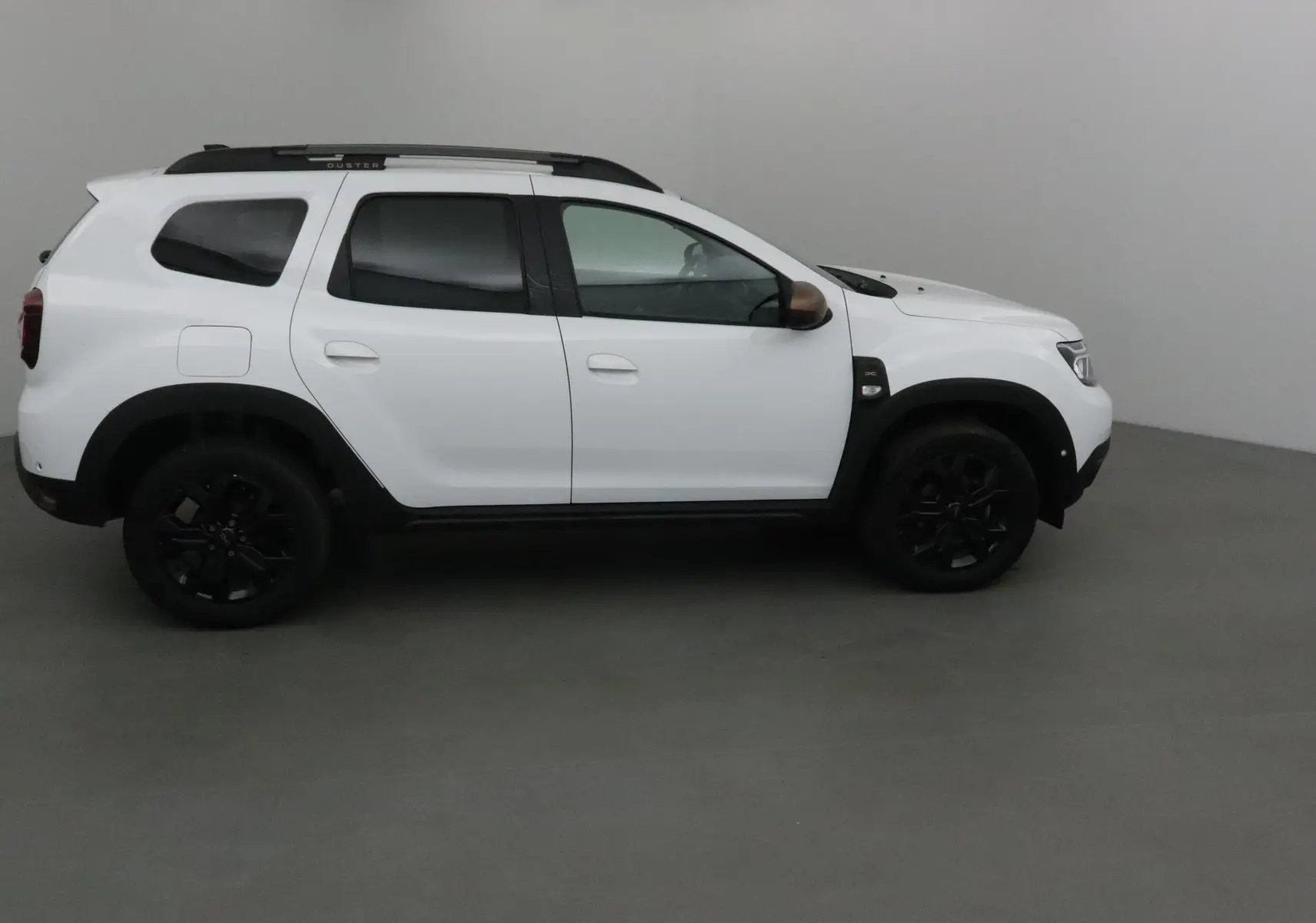 Profil côté gauche du Dacia Duster 4x4 blanc 2024 avec jantes noires et barres de toit noires.