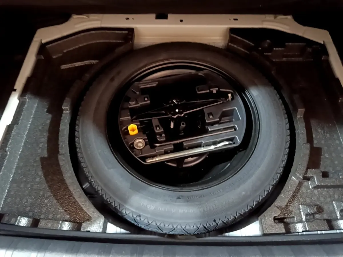 Vue plongeante sur la roue de secours et les outils de bord dans le coffre d'une Peugeot 308 blanche.