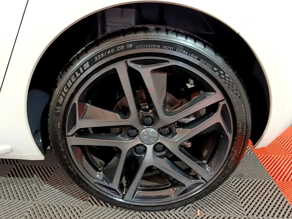 Gros plan sur la roue avant droite noire brillante d'une Peugeot 308 blanche Puretech 130 S&S GT Line 2019.