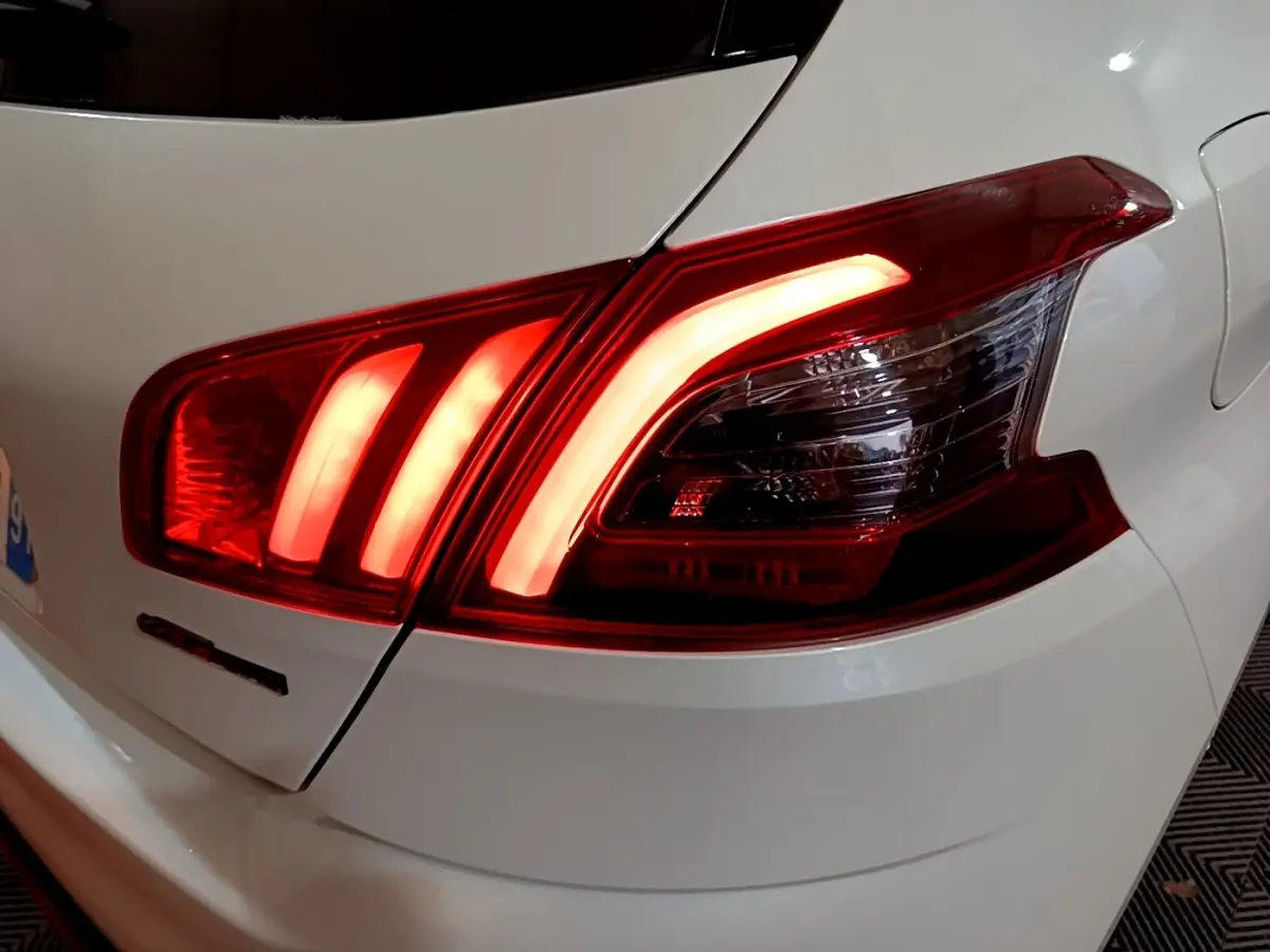 Gros plan sur le feu arrière droit allumé d'une Peugeot 308 blanche, version GT Line, soulignant ses lignes LED distinctives.