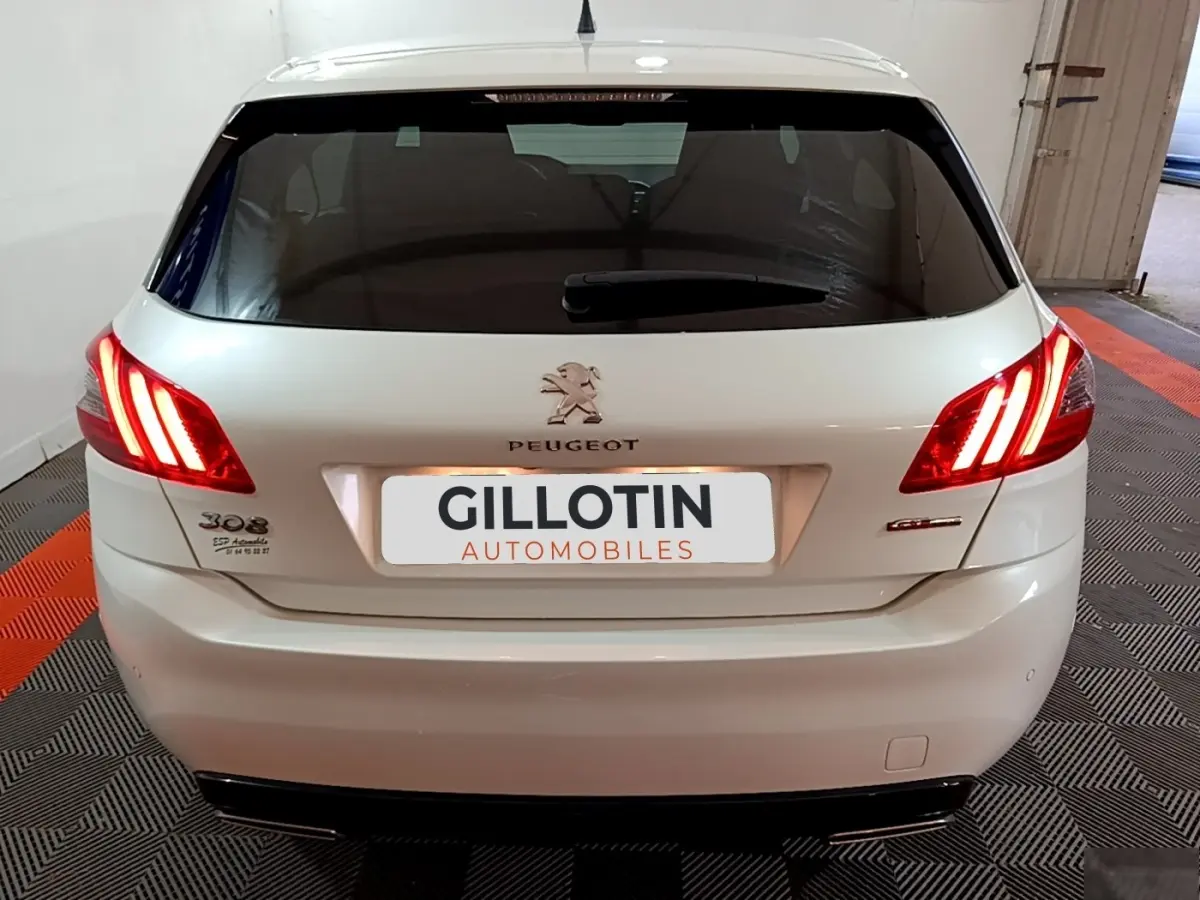 Vue arrière d'une Peugeot 308 blanche avec feux arrière allumés dans un garage fermé.