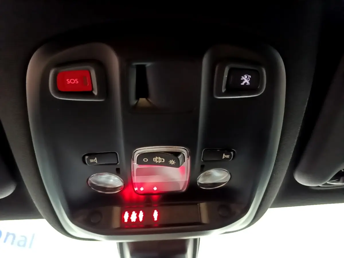 Vue en contre-plongée du plafonnier noir avec bouton SOS rouge et commande d'éclairage dans une Peugeot 308 blanche.