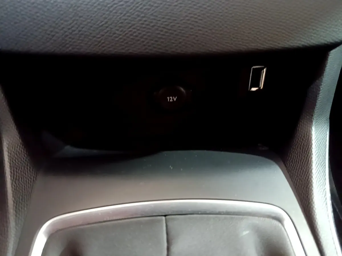 Prise 12V et port USB en gros plan dans l’espace de rangement central d’une Peugeot 308 blanche.