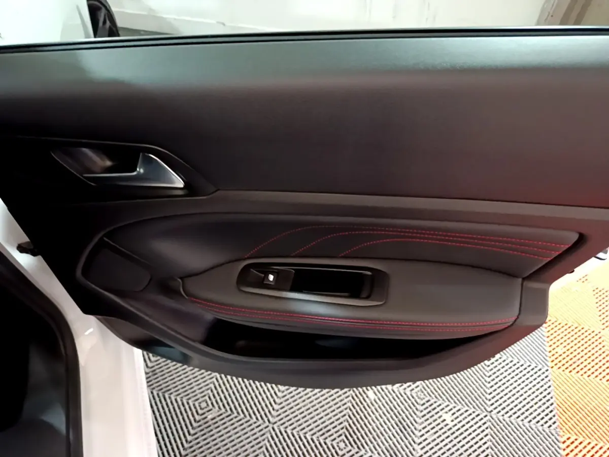 Gros plan sur la porte côté gauche blanche de la Peugeot 308 GT Line avec surpiqûres rouges et commande de vitre.