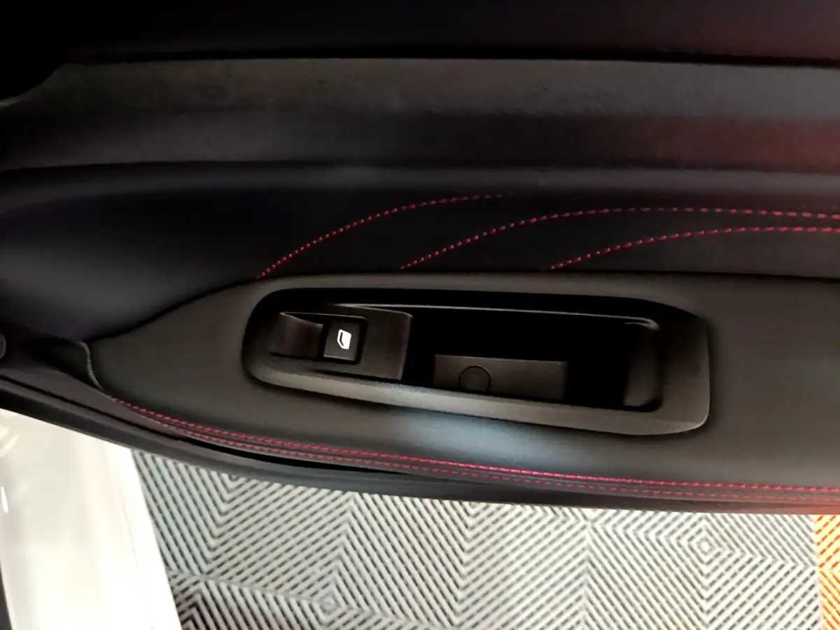 Détail de la poignée intérieure côté gauche avec surpiqûres rouges sur le panneau de porte noir d'une Peugeot 308 GT Line blanche.