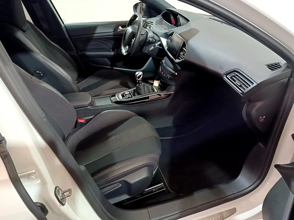Intérieur côté conducteur de Peugeot 308 blanc, montrant sièges noirs avec surpiqûres rouges et tableau de bord moderne.