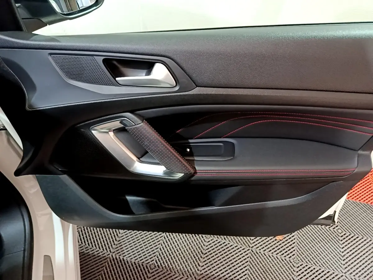 Gros plan sur la porte côté gauche d'une Peugeot 308 GT Line blanche, avec surpiqûres rouges et poignée argentée.