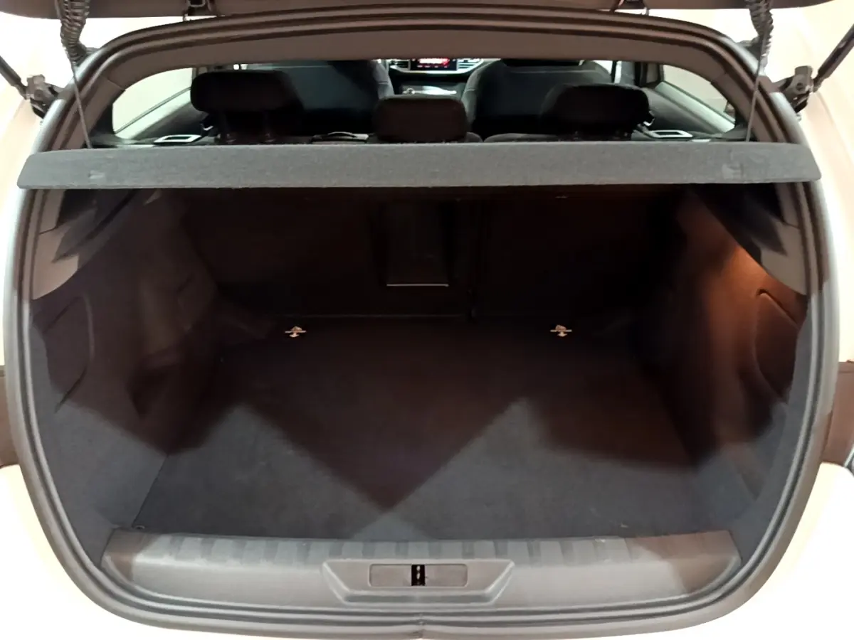 Coffre ouvert d'une Peugeot 308 blanche, vue arrière montrant l'espace de chargement vide et la tablette cache-bagages.