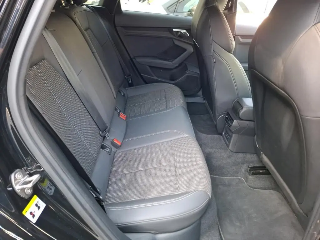 Vue intérieure arrière côté gauche de l'Audi A3 Sportback noire, montrant les sièges arrière en tissu et cuir avec ceintures rouges.