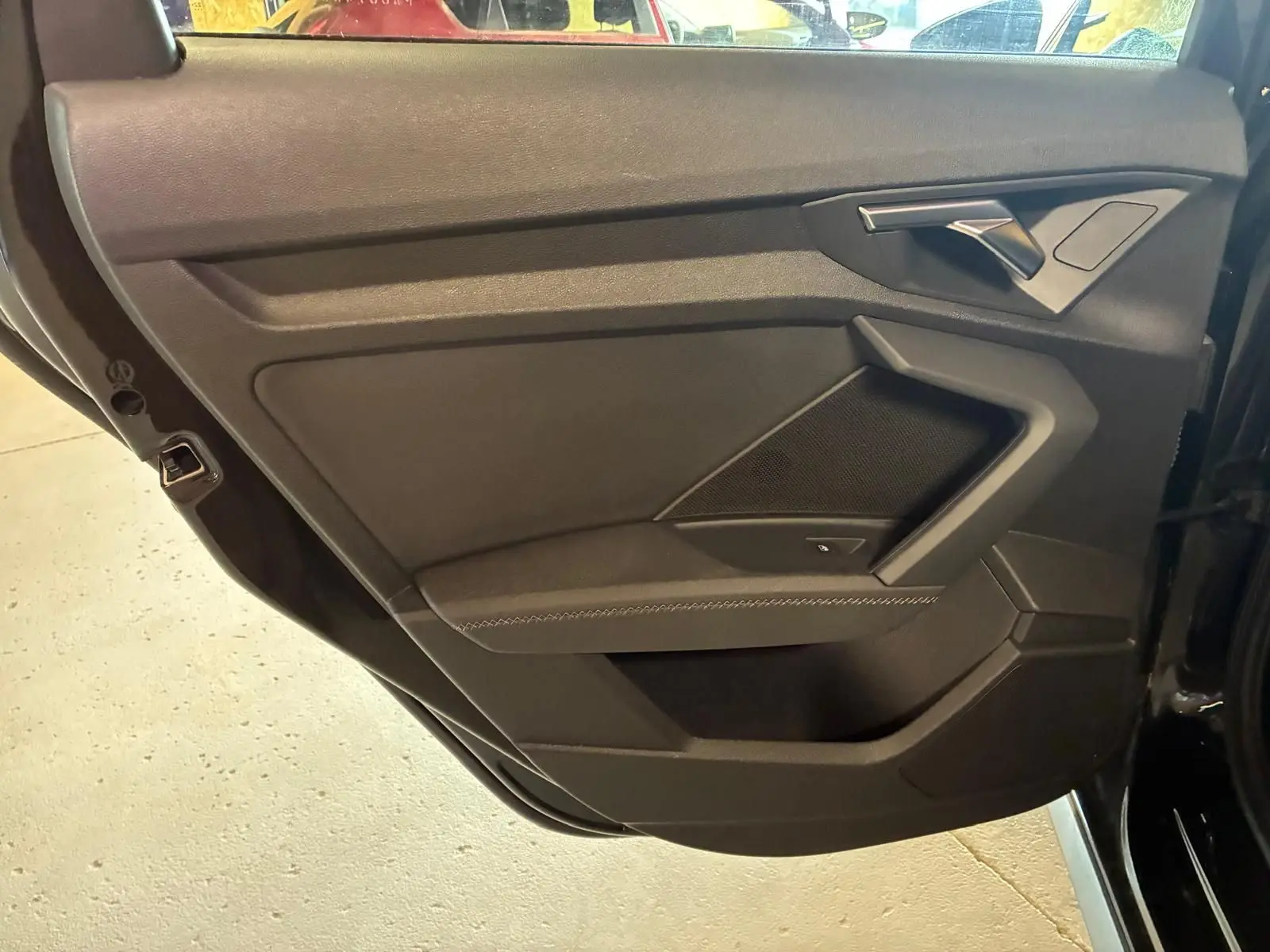 Vue intérieure côté gauche de la porte arrière noire de l'Audi A3 Sportback avec accoudoir en similicuir et poignée argentée.