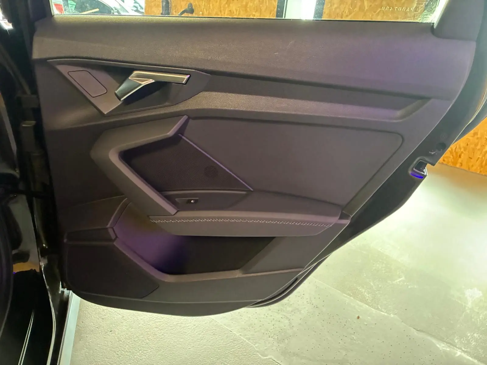 Vue rapprochée de la portière avant gauche noire de l'Audi A3 Sportback 2023 avec accoudoir en similicuir et insert aluminium.
