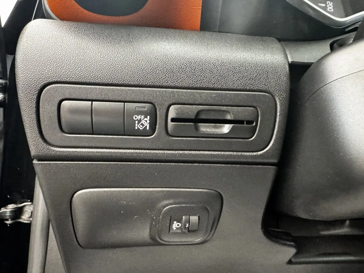 Gros plan sur les commandes latérales noires du tableau de bord d'une Citroën C3 Aircross noire, avec bouton d'assistance et réglage phare.