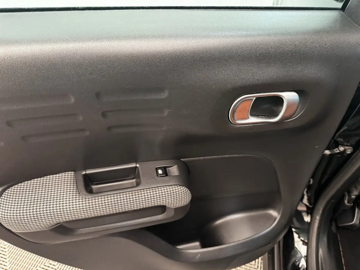 Gros plan sur la porte intérieure côté droit de la Citroën C3 Aircross noire, avec poignée chromée et accoudoir à motif pied-de-poule.