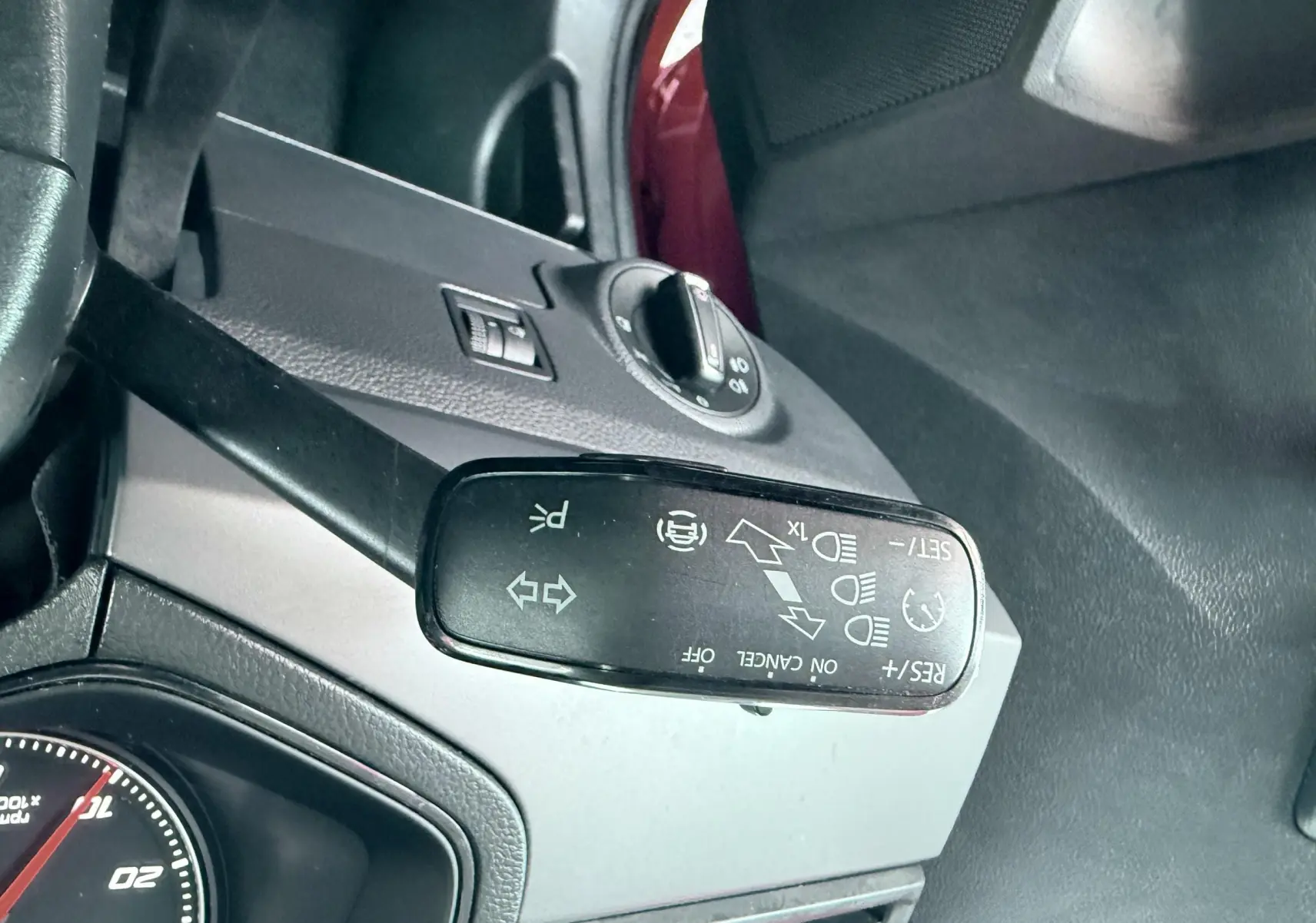 Gros plan sur le commodo gauche du volant d’une SEAT Ibiza rouge passion, avec tableau de bord gris et commandes visibles.