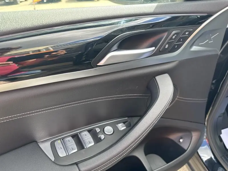 Vue rapprochée de la porte avant gauche noire du BMW X3 xDrive30e 2023 avec commandes électriques et surpiqûres blanches.