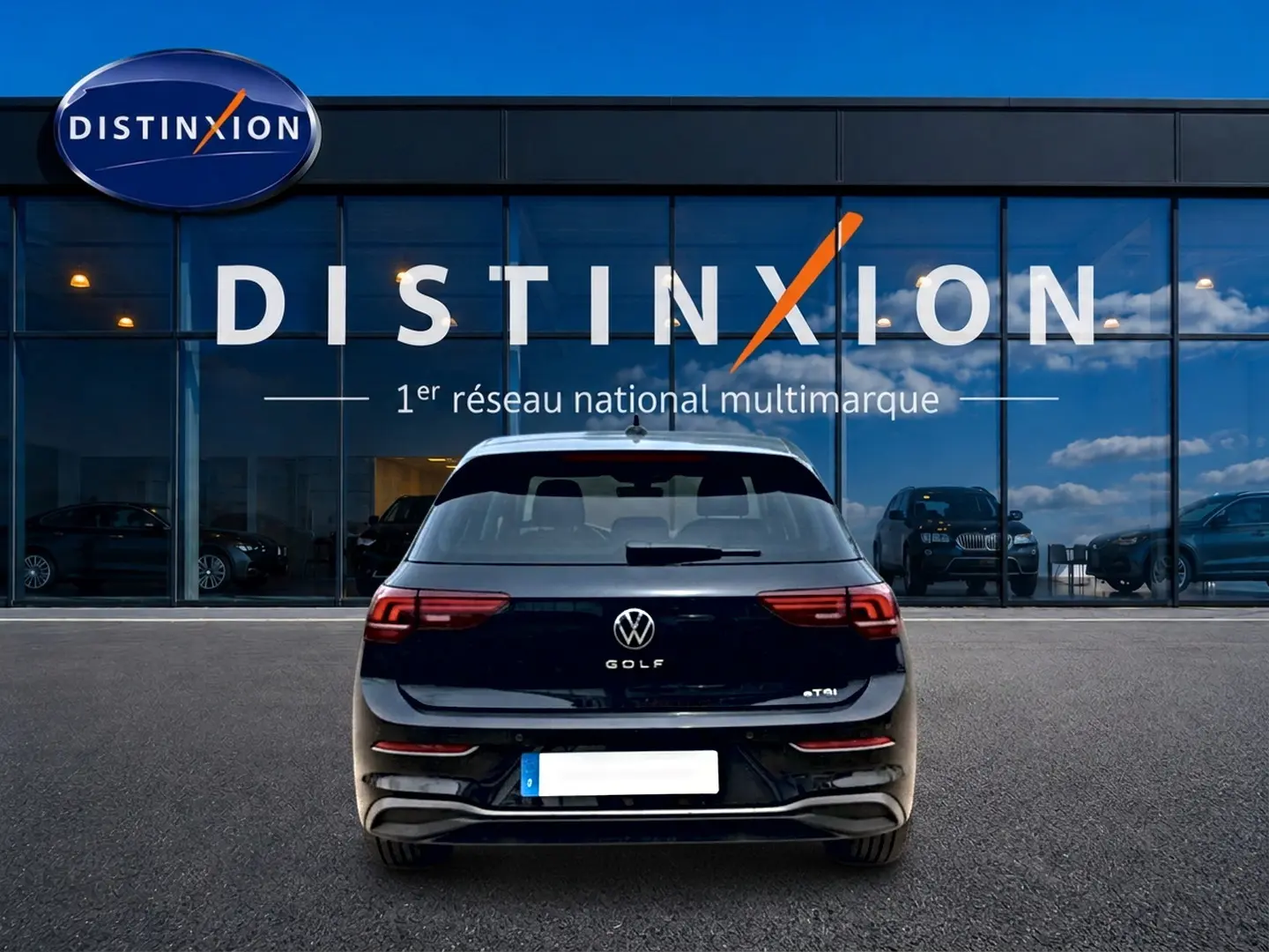 Vue arrière d'une Volkswagen Golf noire 2026 garée devant une vitrine avec logo Distinxion.