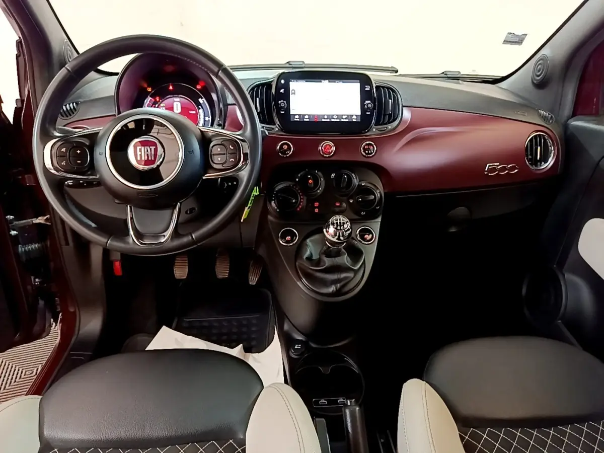 Vue intérieure avant de la Fiat 500 rouge, tableau de bord bordeaux avec écran tactile et volant cuir multifonctions.