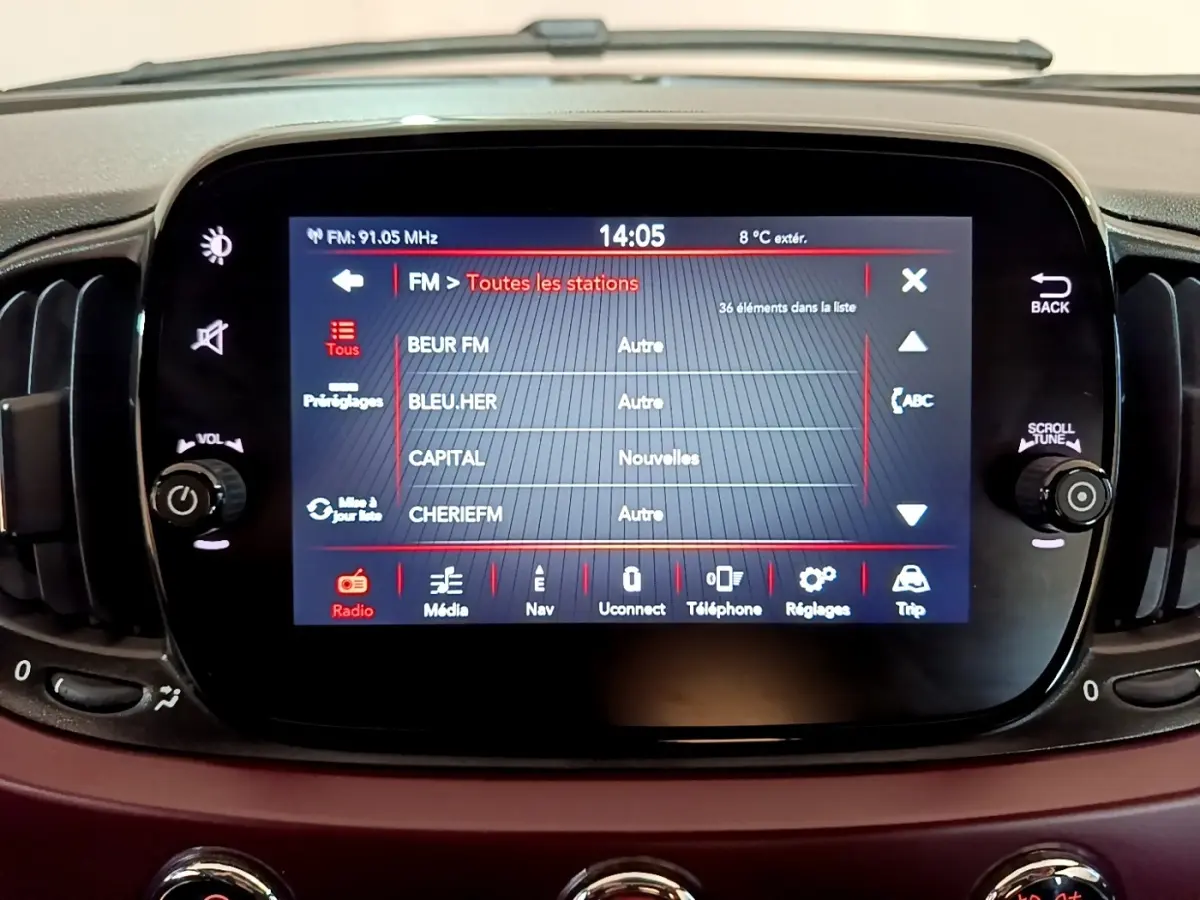 Écran tactile central de la FIAT 500 rouge de 2021 affichant la liste des stations radio FM.