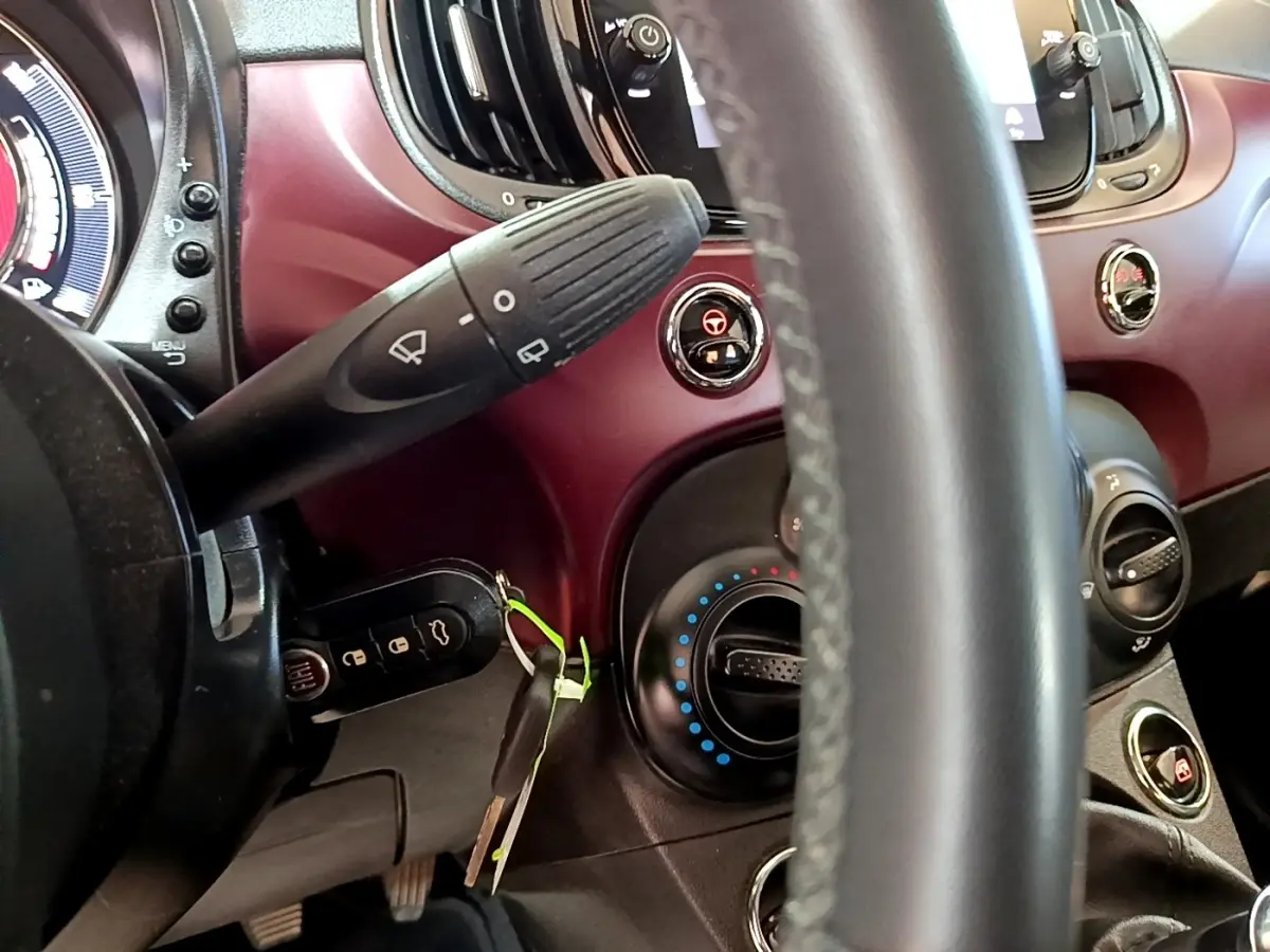 Vue rapprochée du tableau de bord rouge de la Fiat 500 1.0 70ch BSG Star, volant cuir et commandes visibles.