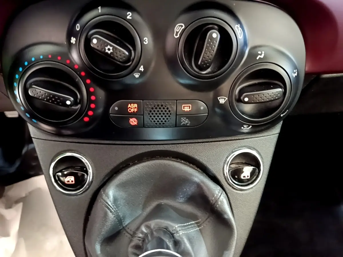 Gros plan sur les commandes de climatisation et la soufflet de levier de vitesse en cuir noir de la FIAT 500 rouge.