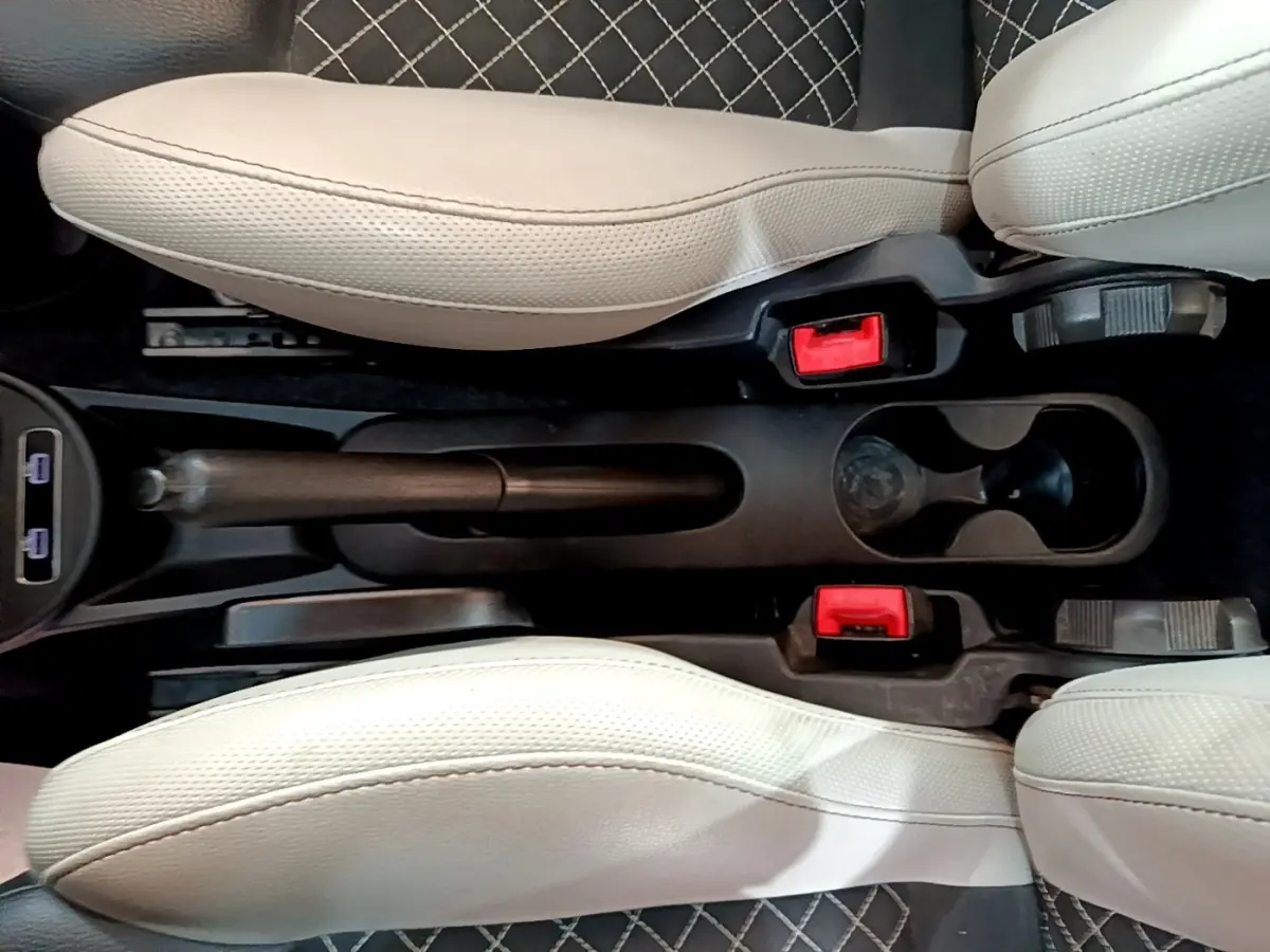 Vue plongeante sur la console centrale noire entre les sièges beige clair d'une Fiat 500 1.0 hybride, avec frein à main manuel et deux porte-gobelets.