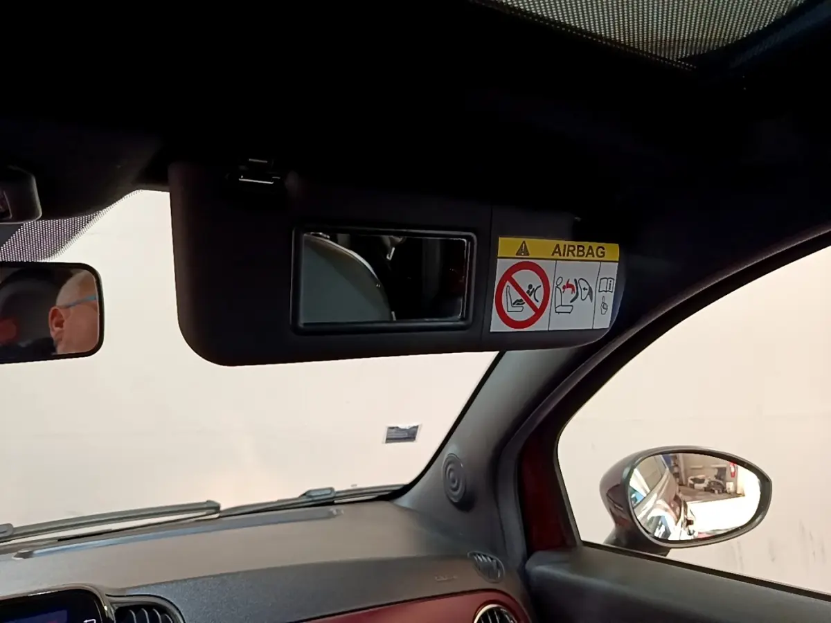 Détail intérieur montrant le pare-soleil avec miroir et avertissement airbag, côté conducteur d'une FIAT 500 rouge.