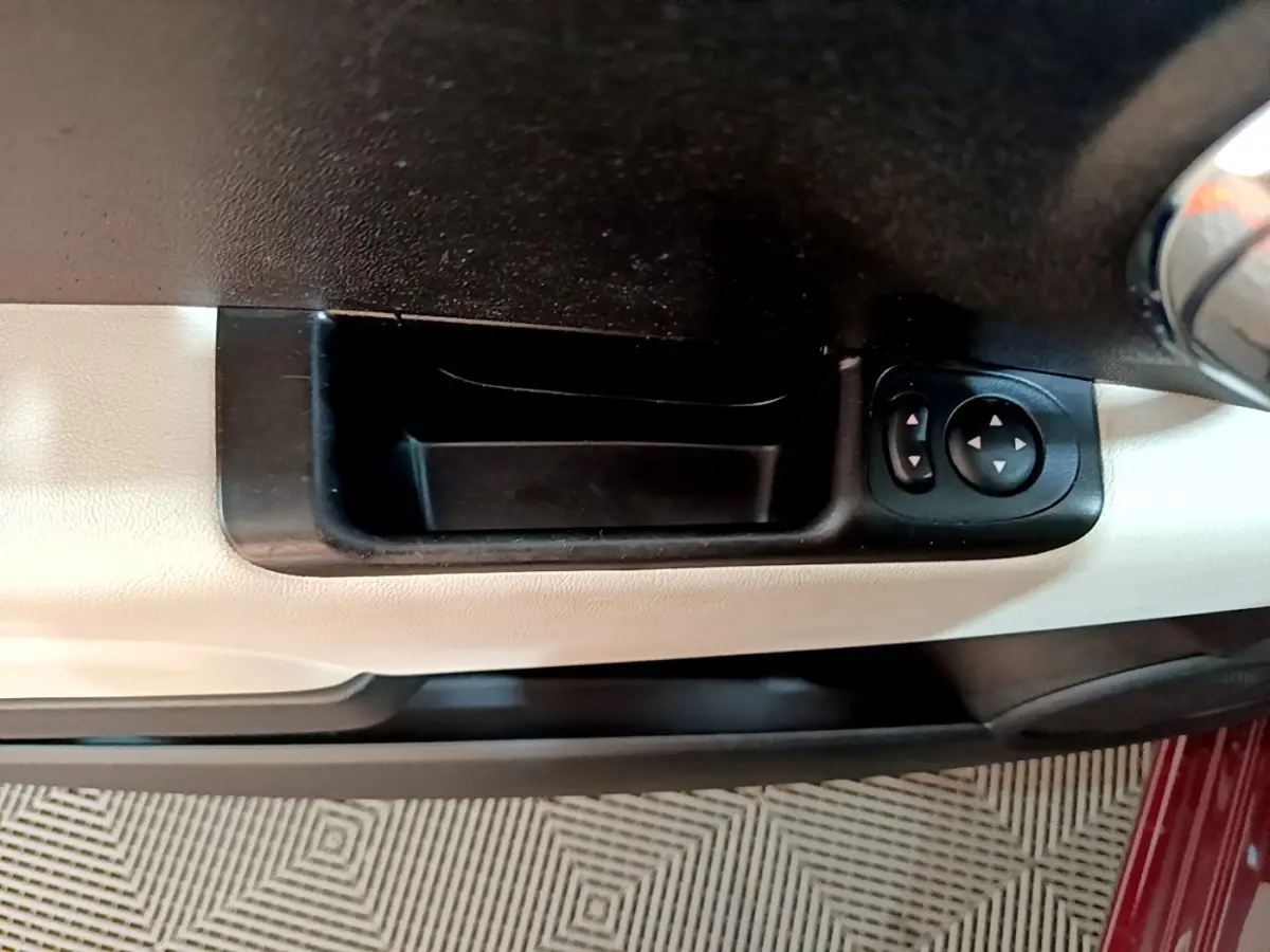 Poignée intérieure côté gauche avec commandes des rétroviseurs sur porte beige d'une FIAT 500 rouge 2021.