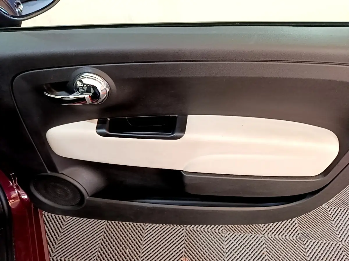 Intérieur de la porte côté gauche de la Fiat 500 rouge, avec poignée chromée et panneau beige contrastant.