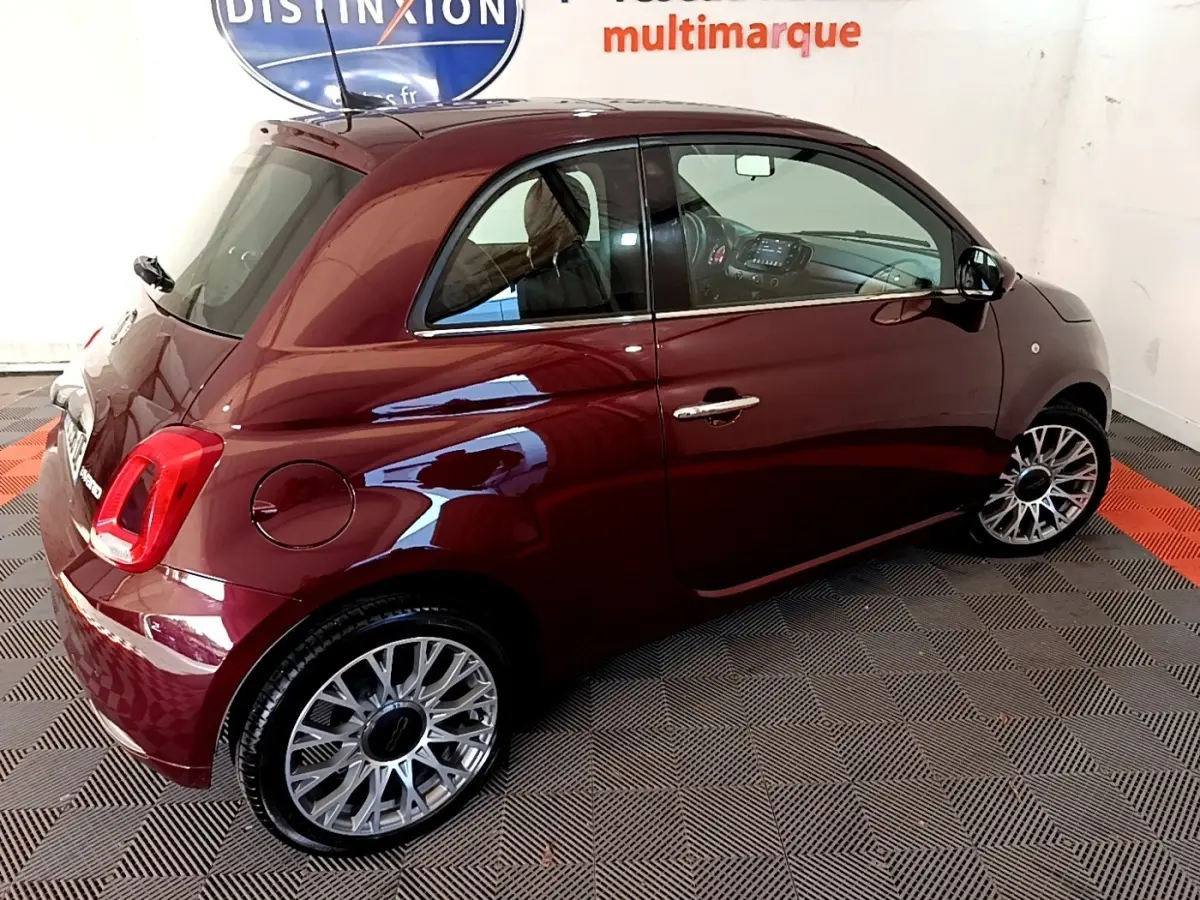 Vue 3/4 arrière droite d'une FIAT 500 rouge brillante avec jantes alliage et intérieur visible par la vitre.