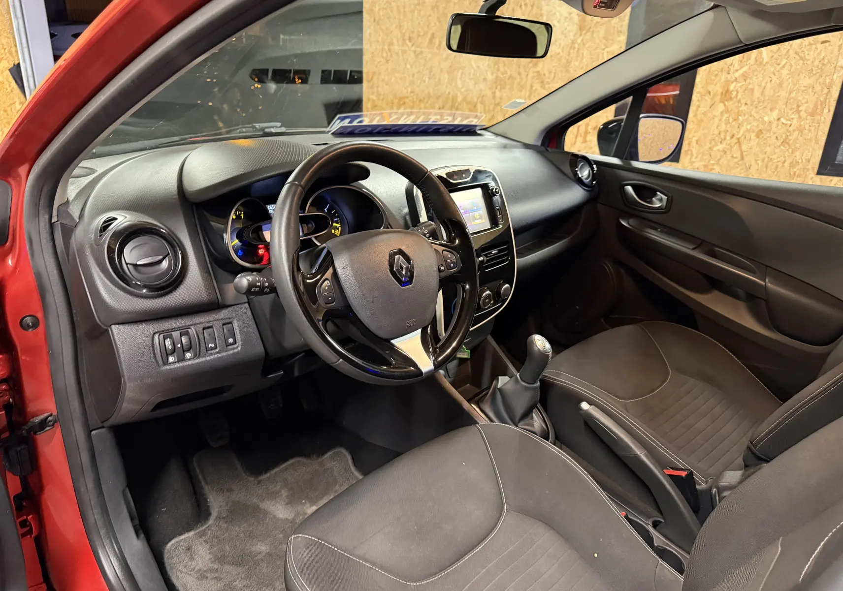 Intérieur côté conducteur d'une Renault Clio Estate IV rouge, montrant le tableau de bord et la boîte manuelle.
