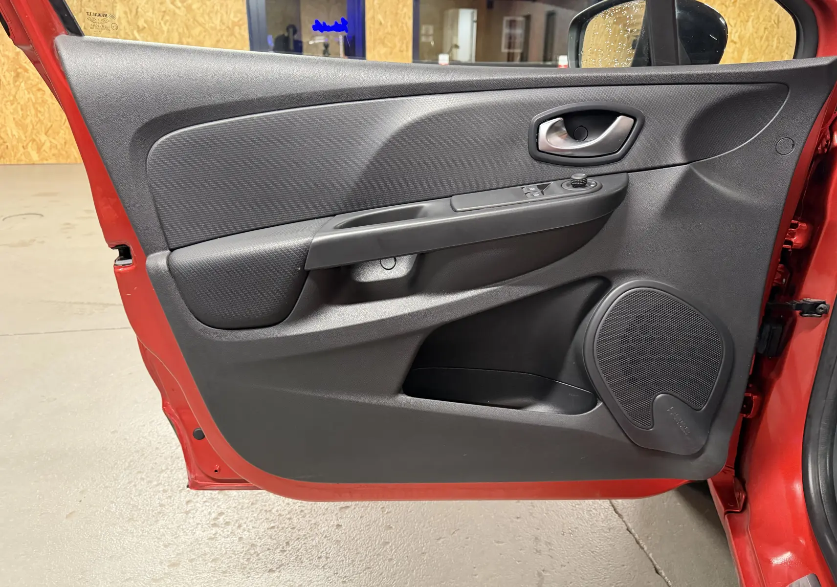 Porte avant gauche ouverte d'une Renault Clio Estate IV rouge, montrant la garniture intérieure noire avec commandes électriques.