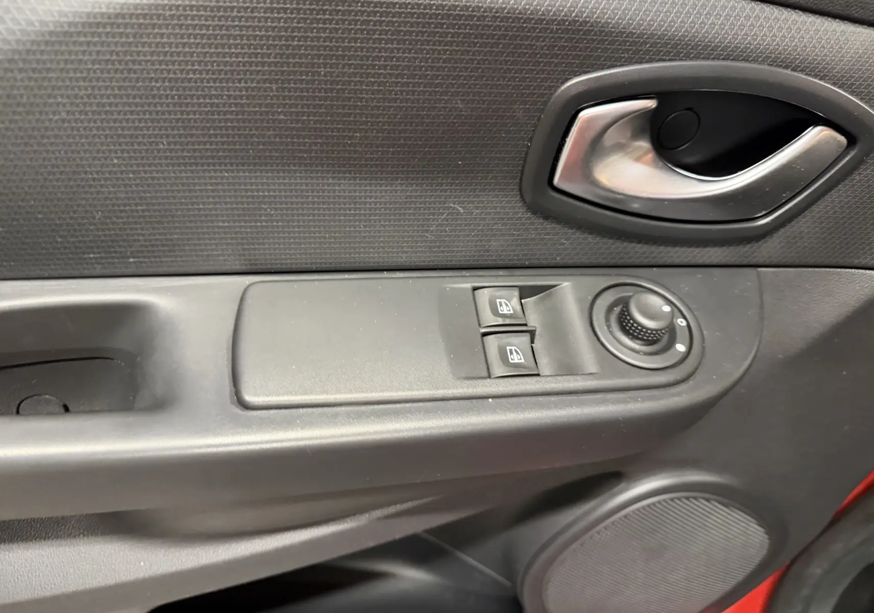 Gros plan sur la commande des vitres et le bouton de réglage des rétroviseurs côté conducteur d'une Renault Clio Estate IV rouge.