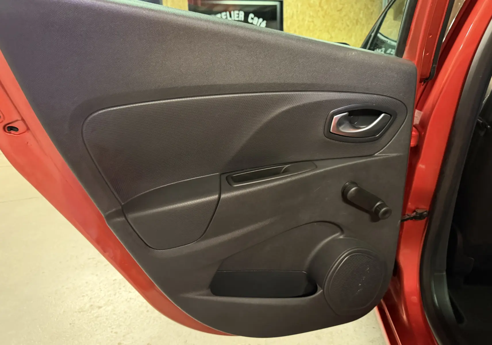 Gros plan sur la porte avant gauche rouge d'une Renault Clio Estate IV 2015 avec manivelle de vitre et poignée intérieure.