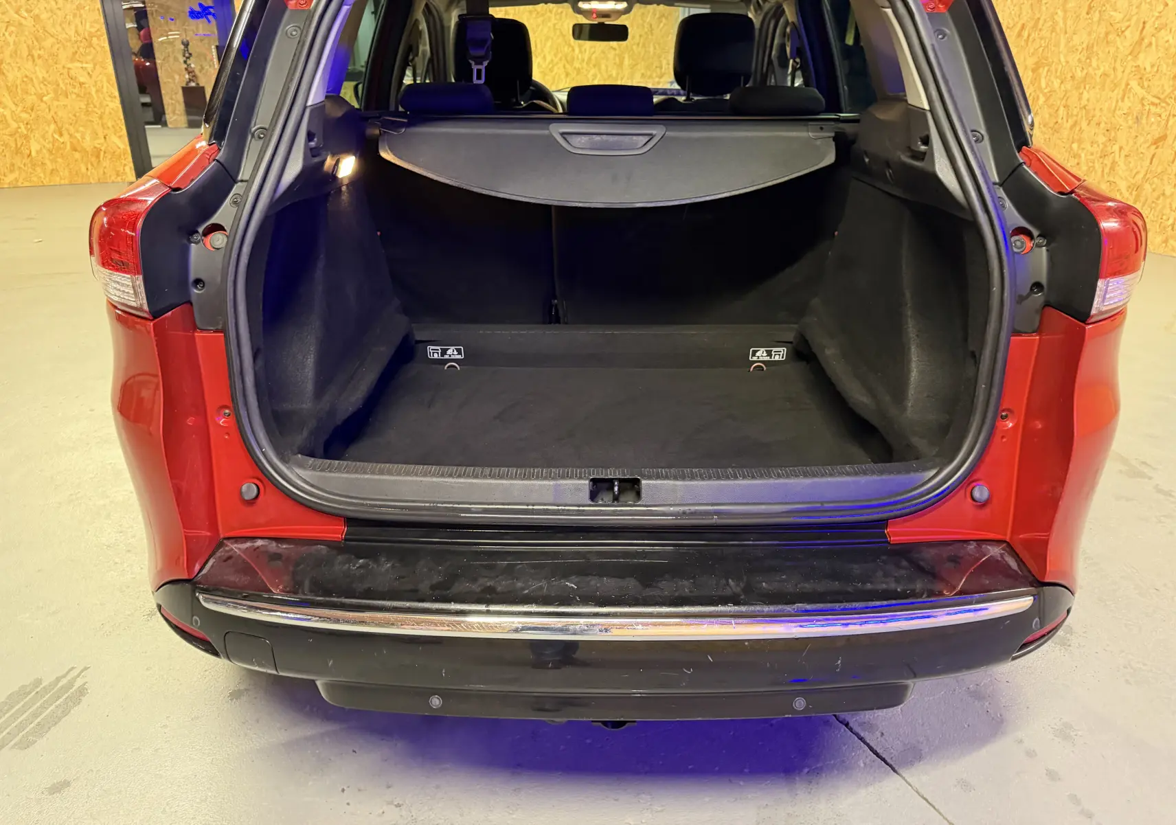 Coffre ouvert vu de l'arrière d'une Renault Clio Estate IV rouge, montrant l'espace de chargement vide et la plage arrière.