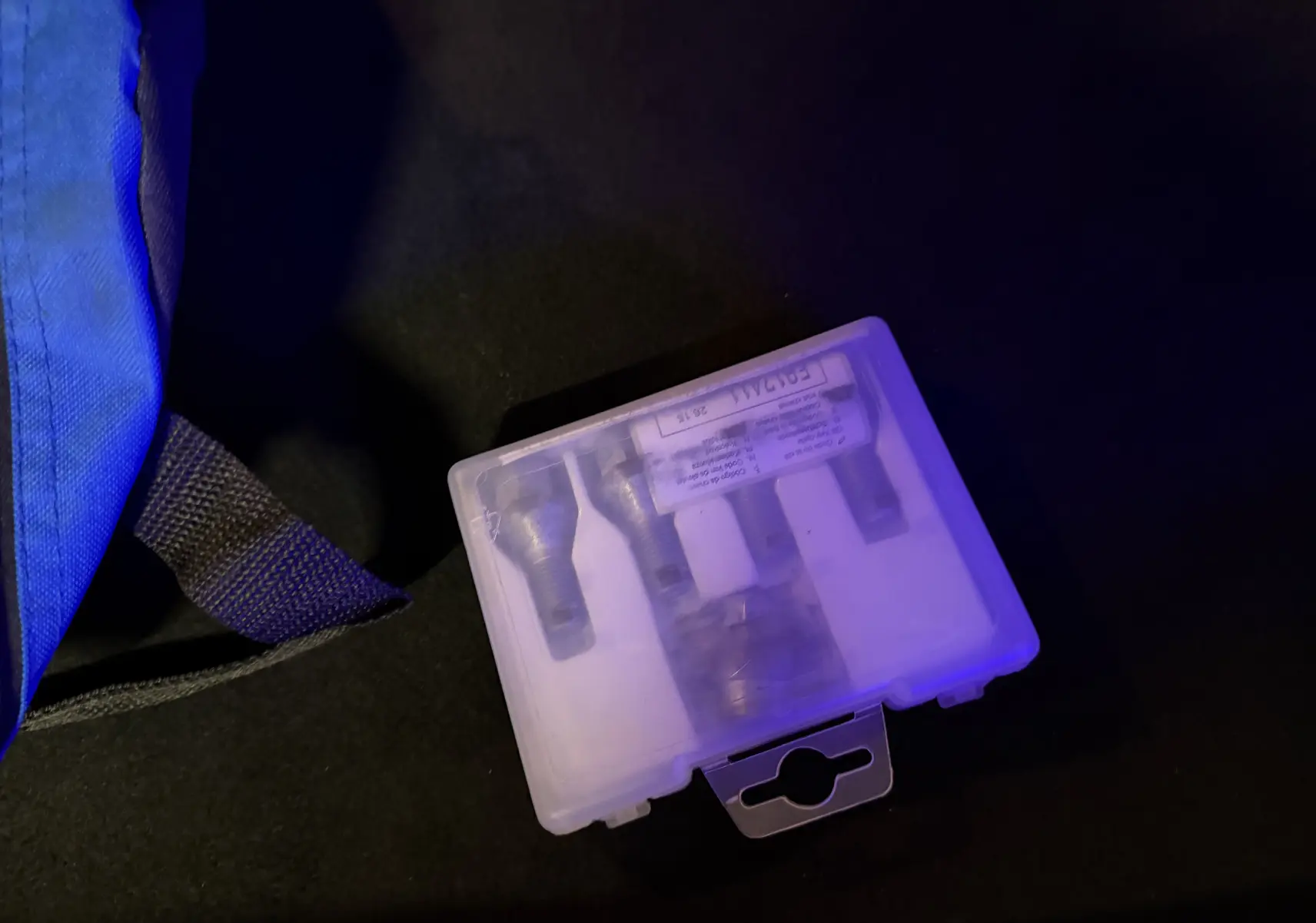 Boîtier transparent contenant des écrous antivol posé dans le coffre d'une Renault Clio Estate IV rouge.