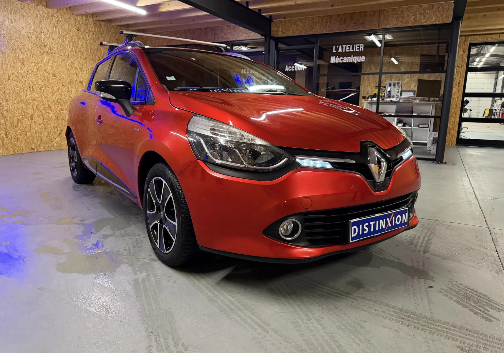 Renault Clio Estate IV rouge vue 3/4 avant droit avec barres de toit et jantes alliage noires.