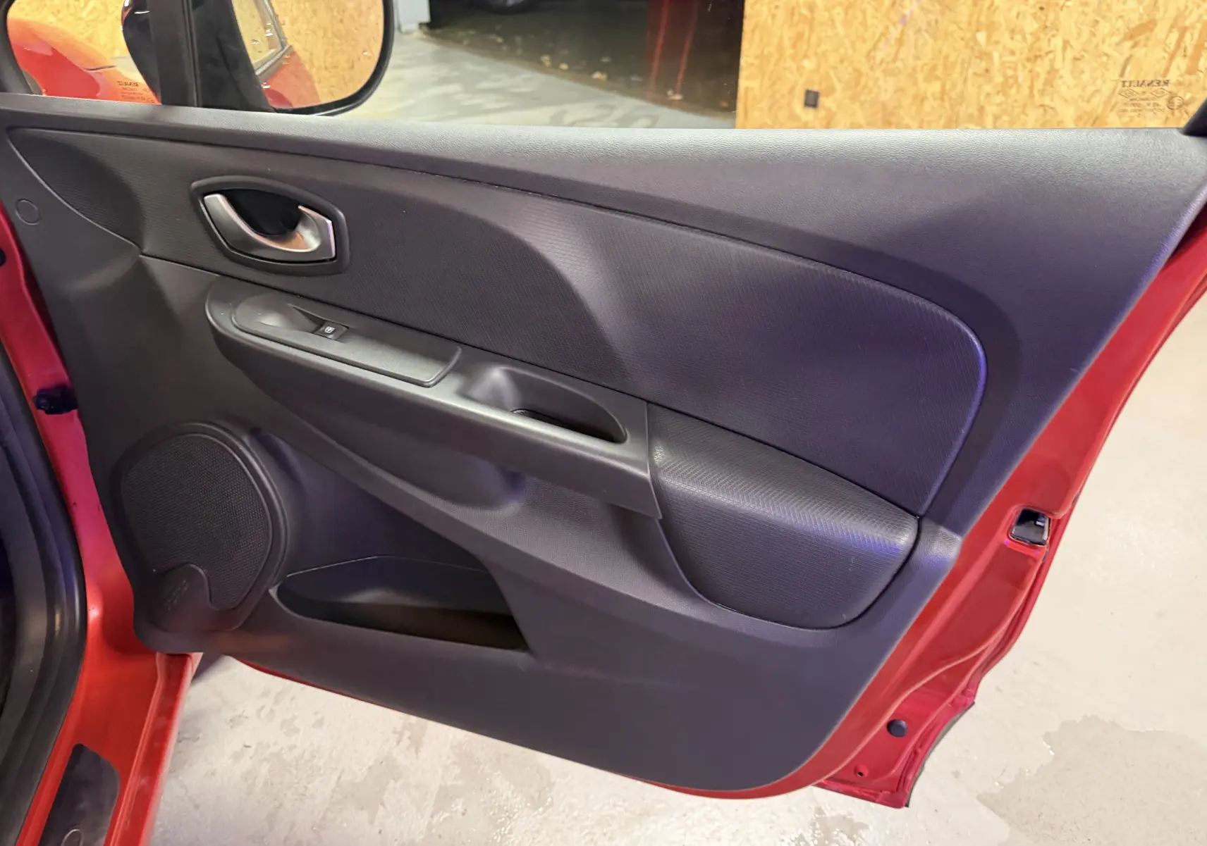 Vue intérieure de la porte avant gauche rouge d'une Renault Clio Estate IV 2015 avec poignée et haut-parleur intégrés.