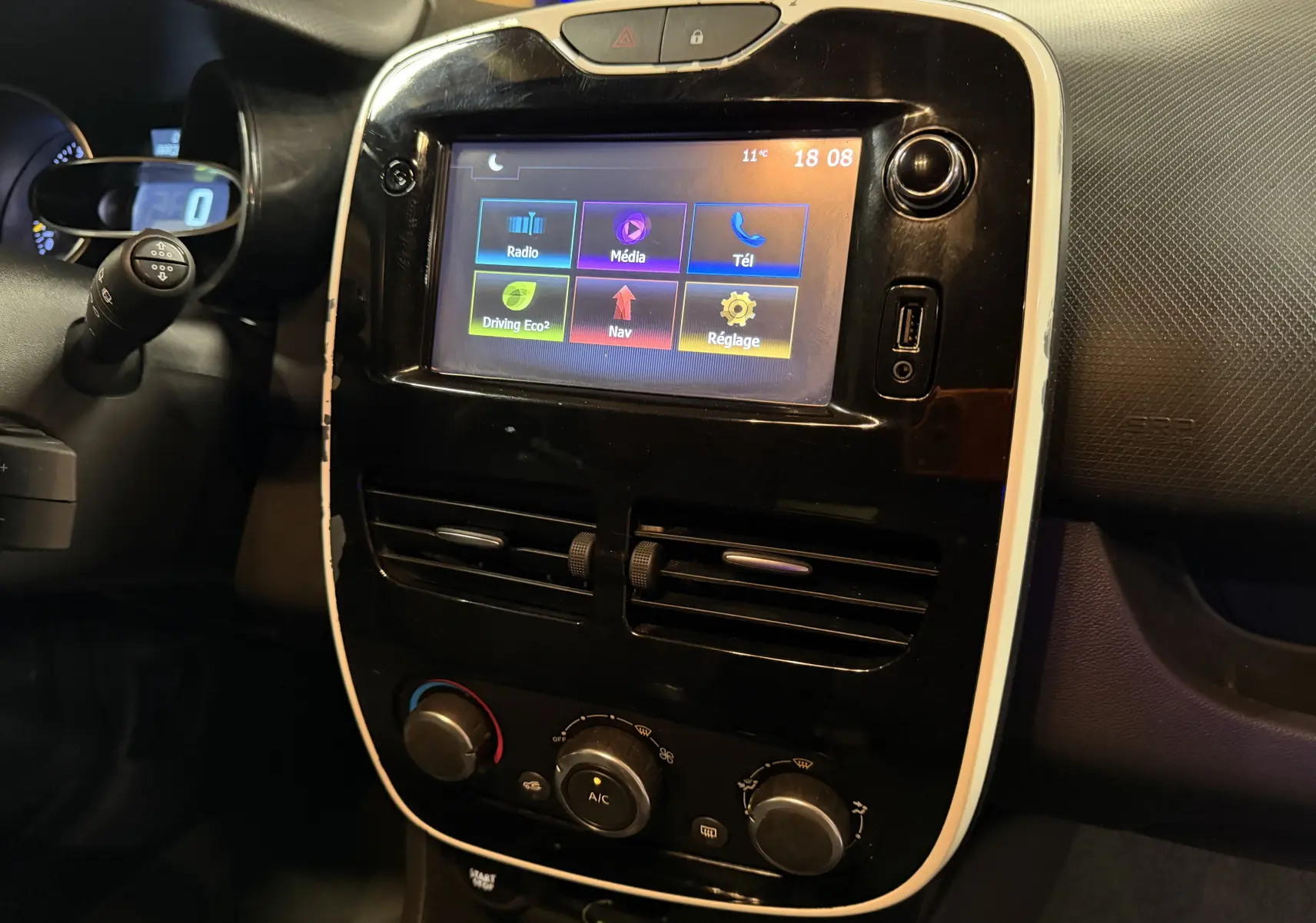 Vue rapprochée de la console centrale noire et blanche avec écran tactile et commandes climatisation d'une Renault Clio Estate IV rouge.